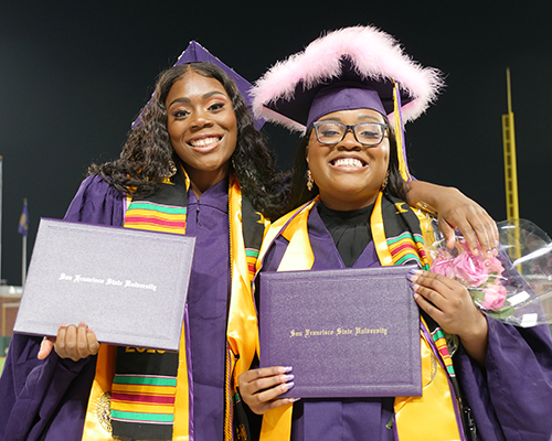 Two grads smiling holding diploma covers 