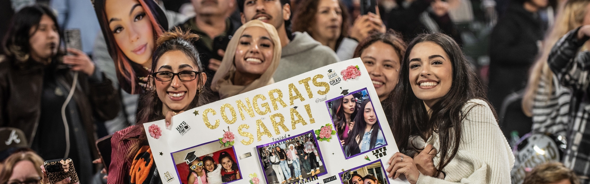 A group of people hold up a poster collage of in Support of Sarah on her graduation day